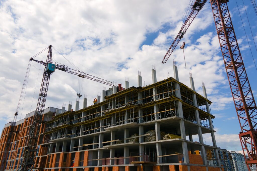 Tower crane at high concrete residential building under construction. Real estate development